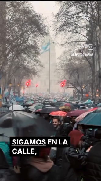 Multitud bajo la lluvia con paraguas y una bandera argentina. Texto: 